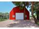 Exterior shot of a vibrant red barn with a white garage door, nestled among mature trees at 17730 E Brooks Farm Rd, Gilbert, AZ 85298