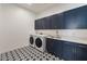 Well-lit laundry room includes black and white patterned floor tiles and navy blue cabinets at 22991 E Via De Olivos --, Queen Creek, AZ 85142