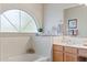 Bright bathroom featuring a large arched window, soaking tub, and wooden vanity at 630 W Navarro Ave, Mesa, AZ 85210
