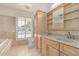 Bright bathroom with dual sinks, travertine tile walls and floors, and a window with plantation shutters at 6550 N 7Th St, Phoenix, AZ 85014
