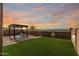 Wide view of the backyard and sunset showcasing the pergola, turf and desert landscaping at 17532 W Copper Ridge Dr, Goodyear, AZ 85338