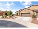 A charming tan home features a three-car garage and a well-manicured front yard with desert landscaping at 20426 N Blazing Sun Rd, Maricopa, AZ 85138