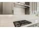 Close up on kitchen range with stainless steel hood, white backsplash, quartz countertops, and gray cabinets at 26914 W Renee Dr, Buckeye, AZ 85396