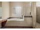 Bright bathroom boasts a soaking tub, tiled shower, vanity, and glass block window at 9715 E Allison Way, Scottsdale, AZ 85262