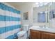 Clean bathroom featuring a blue and white striped shower curtain, toilet, and vanity with wood cabinets at 45543 W Guilder Ave, Maricopa, AZ 85139