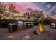 Well-equipped outdoor kitchen with a built-in grill, bar seating, and desert landscaping under a colorful sky at 5690 E Canyon Creek Cir, Carefree, AZ 85377