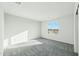 Sunlit bedroom with plush gray carpet, neutral walls, and a window that overlooks a vacant lot under a bright blue sky at 22387 S Manzanilla Rd, Buckeye, AZ 85326