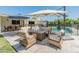 Inviting backyard patio area with comfortable seating around a gas fire pit, umbrellas and pool in the background at 5711 E Corrine Dr, Scottsdale, AZ 85254