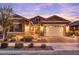 Charming single-Gathering home featuring a two-car garage, a stone facade, and illuminated landscaping at twilight at 20563 E Carriage Way, Queen Creek, AZ 85142