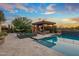 Stunning outdoor pool features a spa, covered patio, and lush landscaping against the backdrop of a colorful sunset at 37440 N 104Th Pl, Scottsdale, AZ 85262