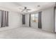 This is a spacious bedroom with light gray walls, plush carpet, a ceiling fan, and three windows with gray curtains at 8010 W Atlantis Way, Phoenix, AZ 85043