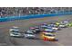 High-speed race cars compete closely on a banked turn, packed with spectators in the background under sunny weather at 9719 W Heber Rd, Tolleson, AZ 85353