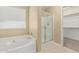 Bright bathroom featuring a white tub, tiled floor, enclosed glass shower, and view into closet at 15420 W Canterbury Dr, Surprise, AZ 85379