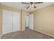 A bedroom featuring neutral walls, carpet, ceiling fan, and a double door closet and entry door at 15420 W Canterbury Dr, Surprise, AZ 85379