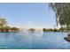 Picturesque community lake view featuring active fountains and lush tree-lined shores under a clear blue sky at 21690 N Lynn St, Maricopa, AZ 85138