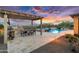 Outdoor oasis featuring a pool, spa, outdoor kitchen, and dining area under a pergola with vibrant sunset backdrop at 5033 N 205Th Gln, Buckeye, AZ 85396