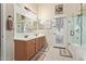 Bright bathroom featuring double vanity, large mirror, and tiled floors leading to shower and decorated glass door at 6002 N 124Th Dr, Litchfield Park, AZ 85340