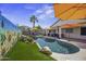 Sparkling pool area surrounded by lush artificial turf, patio seating, and colorful umbrellas at 42760 W Magnolia Rd, Maricopa, AZ 85138