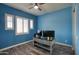 This blue-walled bedroom is staged as an office with a ceiling fan, wood-look floors, and bright, shuttered windows at 18175 W Highland Ave, Goodyear, AZ 85395
