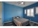 Cozy bedroom featuring a ceiling fan, a comfortable bed, bright, shuttered windows, and light-blue painted walls at 18175 W Highland Ave, Goodyear, AZ 85395