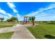 Bright, colorful playground equipment sits on a green lawn under a clear blue sky with scattered clouds at 11501 N Pablo St, El Mirage, AZ 85335