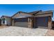 A two-car garage features stone accents, gray doors, and a paved driveway under a bright, clear blue sky at 18204 W Hess St, Goodyear, AZ 85338