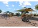 Community playground featuring multiple play structures, swings and shaded awnings on a sunny day at 38115 W Excussare Way, Maricopa, AZ 85138