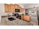 Kitchen with a granite countertop, black appliances, and light wood cabinets; a view into the living room at 16222 W Augusta Ave, Litchfield Park, AZ 85340