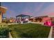 Backyard at dusk featuring artificial grass, pergola, outdoor kitchen, and lighted plants and fencing at 8127 E June St, Mesa, AZ 85207