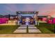 Backyard at dusk featuring artificial grass, fireplace, pergola, outdoor kitchen, and lighted plants and fencing at 8127 E June St, Mesa, AZ 85207