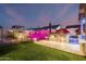Backyard at dusk with an artificial lawn, outdoor kitchen and bar, and lighted plants and fencing at 8127 E June St, Mesa, AZ 85207