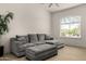 Comfortable living room featuring a large gray sofa, a large window, light wood floors and a modern ceiling fan at 8156 E Questa Rd, Scottsdale, AZ 85255