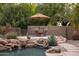 Backyard pool features a rock waterfall, dining area, mature trees and drought tolerant landscaping at 9913 E Quarry Trl, Scottsdale, AZ 85262