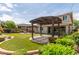 Lush backyard featuring a covered patio, manicured lawn, colorful flowers, and a pergola for outdoor relaxation at 14674 W Pasadena Ave, Litchfield Park, AZ 85340