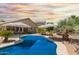 A refreshing backyard swimming pool surrounded by desert landscaping, umbrellas, and loungers at 43036 W Anne Ln, Maricopa, AZ 85138