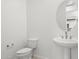 Clean powder room featuring a white pedestal sink, round mirror, and modern toilet at 17837 W Mission Ln, Waddell, AZ 85355