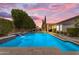 Backyard pool with waterfall feature, lush trees, and outdoor seating area, set against a vibrant sunset sky at 6870 S Justin Way, Chandler, AZ 85249