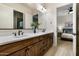 A bright bathroom with double vanity, wooden cabinets, and tile floors, with a glimpse of a bedroom through the open door at 35971 N Prickley Pear Rd, Cave Creek, AZ 85331