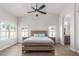 Airy main bedroom with a ceiling fan, wood-look floors, shutters, and an arched entry to the ensuite bathroom at 9566 E Plana Ave, Mesa, AZ 85212