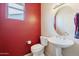 Stylish half bathroom featuring a pedestal sink, round mirror, and textured red wall at 17192 W Hermosa Dr, Surprise, AZ 85387