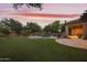 Expansive backyard with a lush lawn, a sparkling pool, and a covered patio, all bathed in the glow of a sunset at 2727 S Balboa Dr, Gilbert, AZ 85295