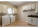 Bright laundry room with white cabinets, granite counters, a round window, and appliances at 3949 E Norcroft Cir, Mesa, AZ 85215