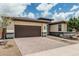 Single-story home showcasing a two-car garage with a brick-paved driveway and desert landscaping at 1272 W Camina Buena Vis, Queen Creek, AZ 85140