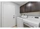 Well-lit laundry room featuring a white washer and dryer set, complemented by dark brown cabinets and a conveniently located door at 1962 E Morrow Dr, Phoenix, AZ 85024
