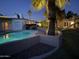 Backyard featuring a pool, palm trees, decorative stone, and a playset, all illuminated at twilight at 3951 E Sequoia Trl, Phoenix, AZ 85044