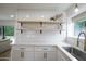 Wet bar area with white cabinets, open shelving, a stainless steel sink, gold faucet, and a window with backyard views at 8425 E Bonnie Rose Ave, Scottsdale, AZ 85250