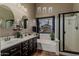Well-lit bathroom featuring a double sink vanity, soaking tub, glass enclosed shower, and a view to the backyard at 29915 N Maravilla Dr, San Tan Valley, AZ 85143