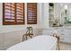 Close-up view of a soaking tub featuring bronze fixtures and a window with wooden shutters at 2527 E Beechnut Ct, Chandler, AZ 85249
