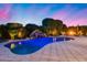 Backyard pool featuring a rock waterfall, cozy seating, and lush landscaping under a vibrant twilight sky at 19414 W Pasadena Ave, Litchfield Park, AZ 85340