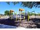 Colorful playground equipment includes climbing structures and slides, set in a rubber mulch and shaded area at 36950 W Mondragone Ln, Maricopa, AZ 85138